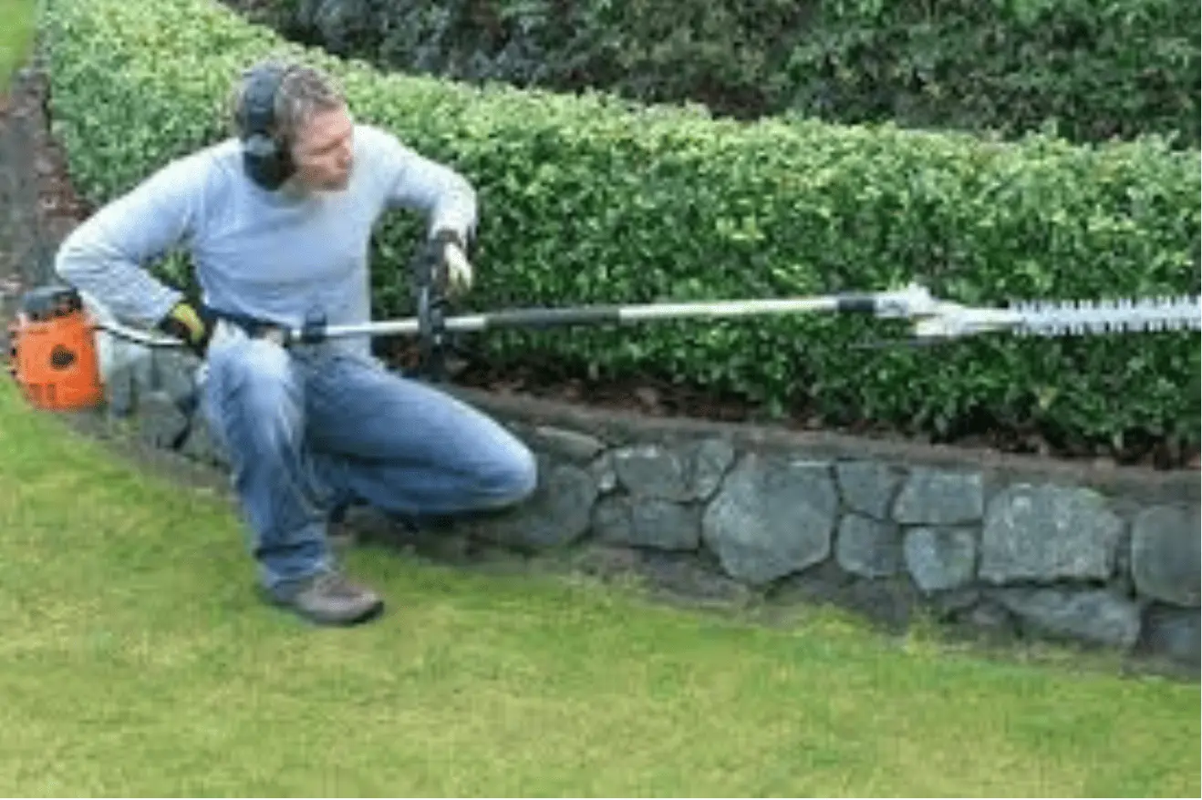 a man cleaning and shaping down the lawn fence made of grass